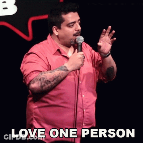 A Man In A Pink Shirt Is Holding A Microphone With The Words Love One Person Above Him GIF