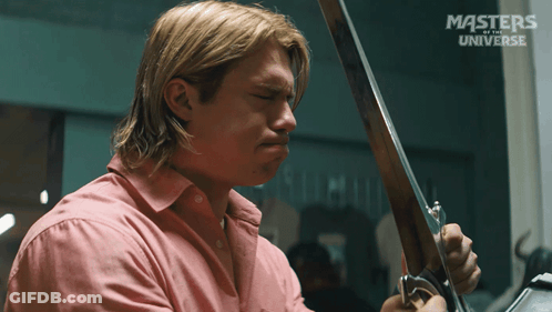 A Man In A Pink Shirt Is Holding A Sword In Front Of A Masters Of The Universe Sign GIF