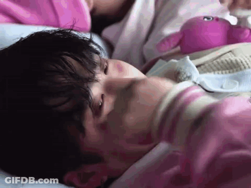 A Man In A Pink Shirt Is Laying In Bed With A Pink Stuffed Animal . GIF