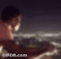 A Man In A Pink Shirt Is Looking Out Over A Body Of Water At Night GIF