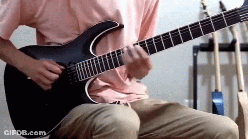 A Man In A Pink Shirt Is Playing A Black Guitar GIF