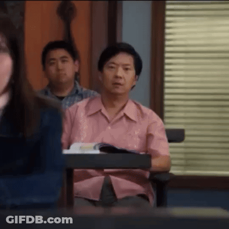 A Man In A Pink Shirt Is Sitting At A Desk In A Classroom With Other Students . GIF