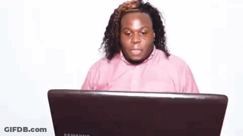 A Man In A Pink Shirt Is Sitting At A Laptop Computer . GIF