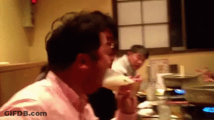 A Man In A Pink Shirt Is Sitting At A Table Drinking A Beer . GIF
