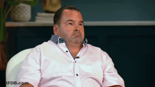 A Man In A Pink Shirt Is Sitting In A Chair And Making A Face GIF