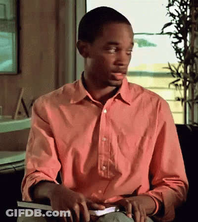 A Man In A Pink Shirt Is Sitting In Front Of A Window Holding A Book GIF