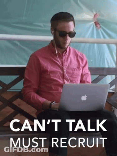 A Man In A Pink Shirt Is Sitting On A Bench Using An Apple Laptop With The Words " Can 'T Talk Must Recruit " Above Him GIF