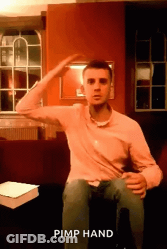 A Man In A Pink Shirt Is Sitting On A Couch And Making A Pimp Hand Gesture . GIF