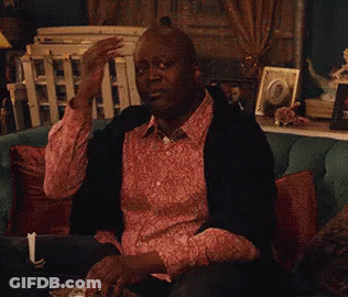 A Man In A Pink Shirt Is Sitting On A Couch Drinking A Glass Of Wine . GIF