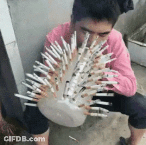 A Man In A Pink Shirt Is Sitting On The Ground Holding A Bowl Of Cigarettes . GIF