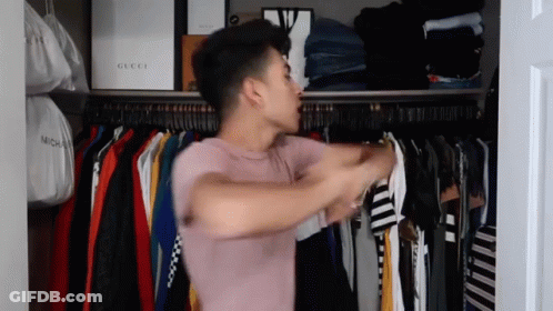 A Man In A Pink Shirt Is Standing In A Closet Filled With Clothes And Bags . GIF