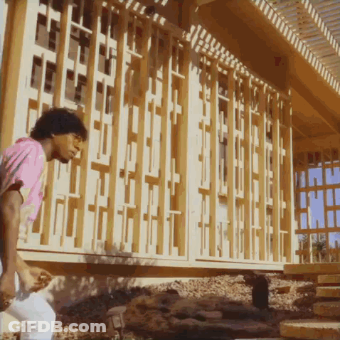 A Man In A Pink Shirt Is Standing In Front Of A Building That Is Being Built GIF