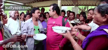 A Man In A Pink Shirt Is Standing In Front Of A Crowd Of People Holding Plates . GIF