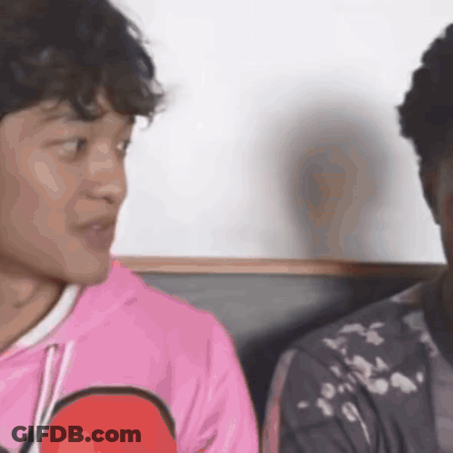 A Man In A Pink Shirt Is Talking To Another Man In A Black Jacket . GIF