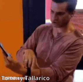 A Man In A Pink Shirt Is Using A Tablet With The Name Tommy Tallarico On The Bottom GIF