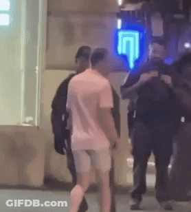 A Man In A Pink Shirt Is Walking In Front Of A Blue Sign That Says ' U ' On It . GIF