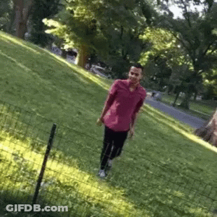 A Man In A Pink Shirt Is Walking Through A Grassy Field GIF