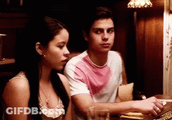 A Man In A Pink Shirt Sits Next To A Woman In A White Tank Top GIF