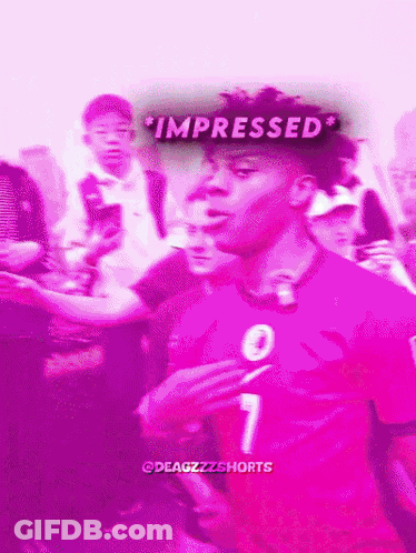 A Man In A Pink Shirt With The Number 7 On It Stands In Front Of A Crowd GIF