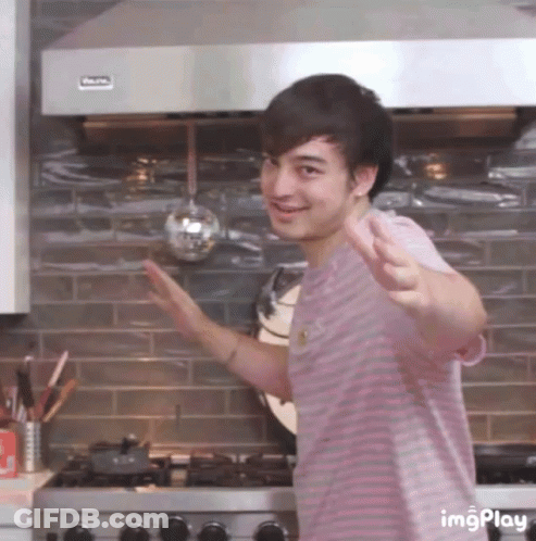 A Man In A Pink Striped Shirt Is Standing In Front Of A Stove With A Ladle Hanging From It .. GIF