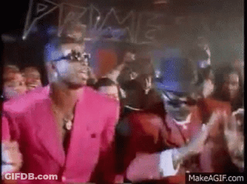 A Man In A Pink Suit And A Man In A Red Suit Are Dancing In Front Of A Crowd . GIF