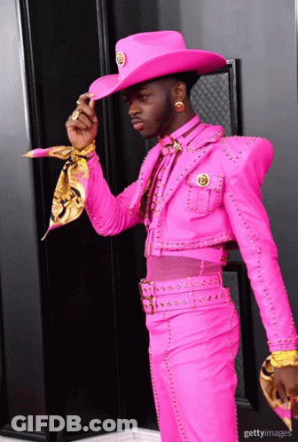 A Man In A Pink Suit And Cowboy Hat Is Standing In Front Of A Black Door GIF