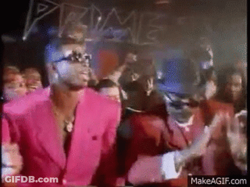 A Man In A Pink Suit Is Dancing In Front Of A Crowd In A Club . GIF