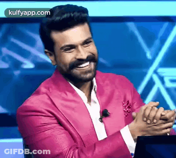A Man In A Pink Suit Is Sitting In Front Of A Laptop And Smiling . GIF
