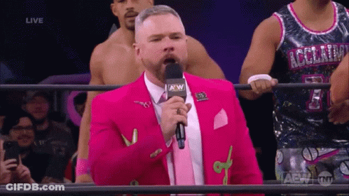 A Man In A Pink Suit Is Speaking Into A Microphone With A Aew Logo GIF
