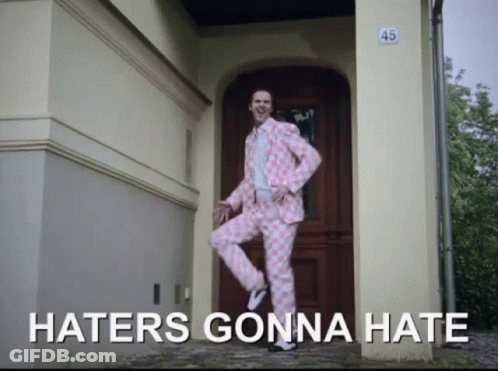 A Man In A Pink Suit Is Standing In Front Of A Door With The Words Haters Gonna Hate Written Below Him GIF