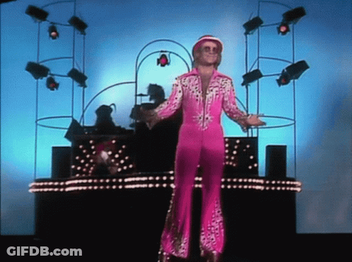 A Man In A Pink Suit Is Standing In Front Of A Stage GIF