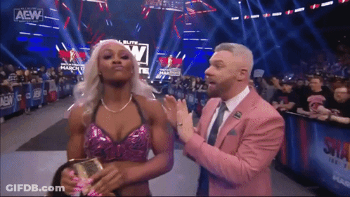A Man In A Pink Suit Is Standing Next To A Woman In A Pink Top . GIF
