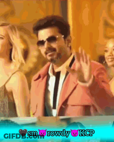 A Man In A Pink Suit Is Waving His Hand In Front Of Two Women GIF