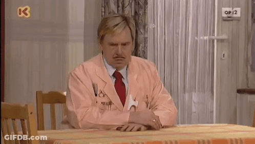 A Man In A Pink Suit Sits At A Table With A Tennis Ball On The Wall Above Him That Says Op12 GIF