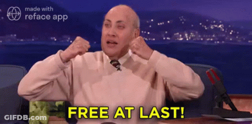 A Man In A Pink Sweater And Tie Is Sitting At A Desk With His Arms In The Air And Says Free At Last . GIF
