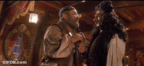 A Man In A Pirate Costume Talks To Another Man In A White Dress GIF