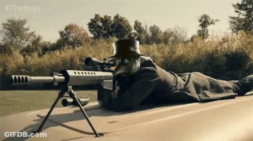 A Man In A Plague Doctor Mask Is Laying On The Ground With A Sniper Rifle GIF