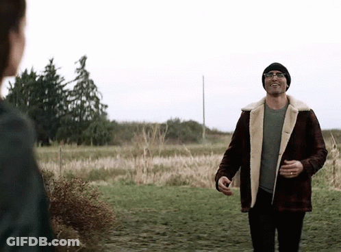 A Man In A Plaid Jacket And A Beanie Is Walking In A Field . GIF