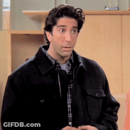 A Man In A Plaid Shirt And A Black Jacket Is Standing In A Room . GIF