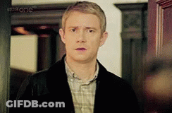 A Man In A Plaid Shirt And A Black Jacket Is Standing In Front Of A Door . GIF