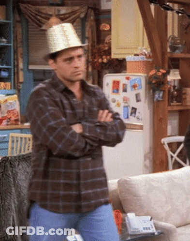 A Man In A Plaid Shirt And A Hat Stands In Front Of A Refrigerator GIF