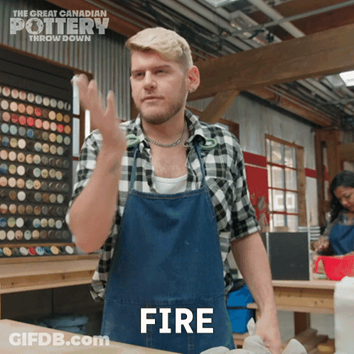 A Man In A Plaid Shirt And Apron Is Making A Fire Gesture GIF