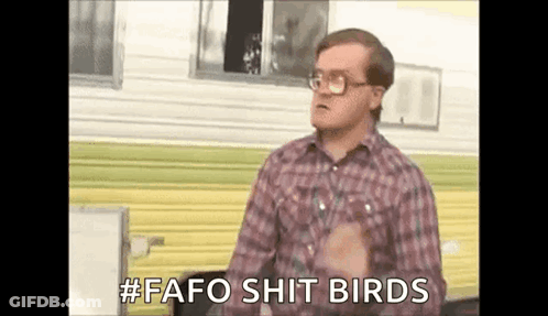 A Man In A Plaid Shirt And Glasses Is Standing In Front Of A Trailer And Talking . GIF