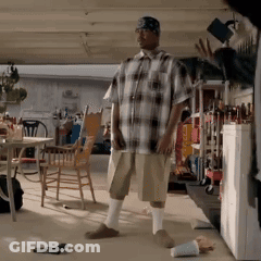 A Man In A Plaid Shirt And Shorts Is Standing In A Garage GIF