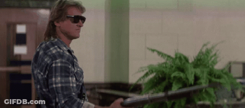 A Man In A Plaid Shirt And Sunglasses Holds A Gun GIF