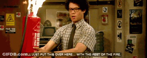 A Man In A Plaid Shirt And Tie Holds A Red Spray Foam Fire Extinguisher In Front Of Him GIF