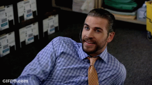 A Man In A Plaid Shirt And Tie Is Laying On The Floor Smiling GIF