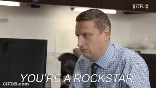 A Man In A Plaid Shirt And Tie Is Sitting At A Desk In Front Of A Computer And Talking . GIF