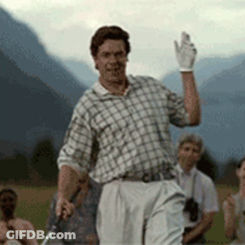 A Man In A Plaid Shirt And White Pants Is Holding A Golf Club And Waving . GIF