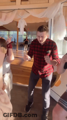 A Man In A Plaid Shirt Is Dancing In Front Of A Window GIF